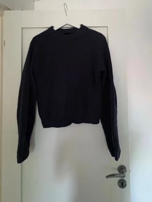 Mörkblå stickad tröja med struktur - Säljer en mörkblå stickad tröja med grov struktur och rund hals. Tröjan har långa ärmar och ribbade muddar vid hals, ärmslut och nederkant. Perfekt för kyliga dagar och enkel att matcha till olika outfits.