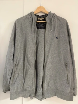 Burberry London Zip Hoodie Grå L - Säljer en Burberry London Zip Hoodie i grå från tidig 2000-tal. Storlek L. I mycket fint skick. Enda anmärkningen är att dragkläppen på dragkedjan saknas, men dragkedjan fungerar utan problem.