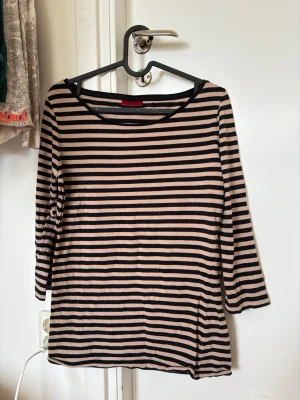 Randig topp från Hugo Boss - Beige och svart randig topp med trekvartsärm och rund halsringning. Mjuk och lätt i materialet.