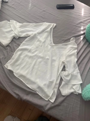 Vit blus med volangärmar - Stilren vit blus i lätt, flowy material med djup v-ringning och dekorativa knytband på axlarna. Aldrig använd 💕