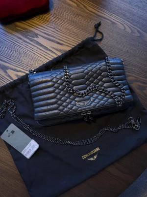 Svart quiltad handväska Zadig & Voltaire - Snygg svart quiltad handväska från Zadig & Voltaire i läder med kedjerem i metall. Väskan har ett elegant mönster, silverfärgade detaljer och logga framtill.