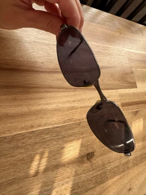 Svarta solglasögon med metallbåge - Snygga solglasögon med mörka, fyrkantiga linser och tunn metallbåge i silver. Klassisk design med svarta skalmar och näskuddar för extra komfort. Perfekta för att höja din stil på soliga dagar.