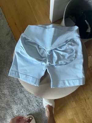 Ljusblå shorts - Säljer ett par ljusblå shorts med hög midja och scrunch-detalj bak. Shortsen är stretchiga och perfekta för träning eller chill. Materialet känns mjukt och följsamt mot kroppen.