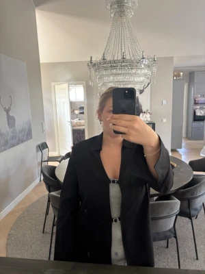 Svart kavaj med enkel knäppning - Stilren svart kavaj med rak passform och enkel knäppning framtill. Klassisk krage och långa ärmar, perfekt för en trendig och clean look. Passar till många olika outfits och är ett måste i garderoben. Materialet ser ut att vara en slät textil.