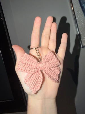Rosa virkad rosett nyckelring - Söt handvirkad nyckelring i form av en rosett i ljusrosa garn. Perfekt att hänga på väskan eller använda till nycklar. Kan virka i vilken färg du vill, bara att höra av dig! (+10kr för custom)