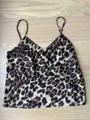 Leopardmönstrad topp - Snygg topp med leopardmönster i bruna och svarta toner. Tunn, glansig och lätt material med smala axelband och v-ringad hals. 