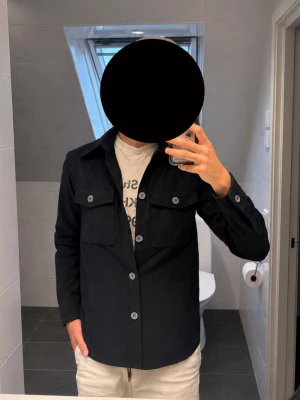 Oscar Jacobson Milron Overshirt Navy - Säljer en Oscar Jacobson Milron Overshirt i mörkblå / marinblå, storlek 48. Använd men i mycket fint skick och har mycket kvar att ge. En stilren overshirt som passar perfekt både som tunn jacka och som ett extra lager över en t-shirt eller skjorta.