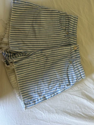 Randiga blåvita highwaist shorts - Snygga blåvita randiga shorts med hög midja och fransiga benslut. Klassisk femficksmodell med knapp och dragkedja framtill. Perfekta för varma dagar och ger en chill vibe till din outfit.