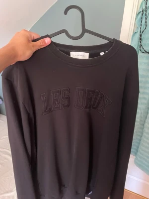 Svart sweatshirt från Les Deux - Svart sweatshirt från Les Deux med broderad logga på bröstet. Tröjan är använd max 2-3 gånger och i nytt skick.