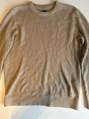 Beige stickad tröja Jack & Jones - Snygg beige stickad tröja från Jack & Jones Originals med rund halsringning och ribbade muddar. Tröjan har ett diskret strukturmönster och är perfekt för lager på lager. Tillverkad i mjukt material som känns skönt mot huden.