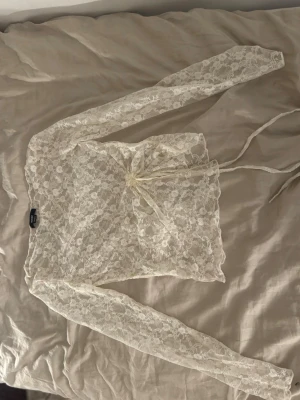 Vit spetsblus med knytband från House - Säljer en tunn, långärmad blus i vit spets från House. Blusen har ett vackert blommönster och knytband i midjan för en snygg siluett. Perfekt för dig som gillar romantisk och feminin stil. Den är storlek S och den är genomsynling. Köpte den utomland den va ganska dyr 