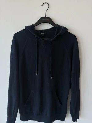 Mörkblå hoodie från Ron Dorff - Mörkblå hoodie från Ron Dorff med klassisk huva och dragsko. Tröjan har känguruficka framtill och ribbade muddar vid ärmslut och nederkant. Tillverkad i mjukt stickat material som känns skönt mot huden. Perfekt för en avslappnad och stilren look.