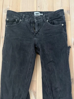 Svarta bootcut jeans från lager 157 - Säljer ett par svarta low waist bootcut jeans från lager 157 med råa kanter nertill. Jeansen har klassisk femficksmodell, dragkedja och knapp i midjan. Materialet är mjukt denim med lite stretch för skön passform. Perfekta till en avslappnad och trendig look.