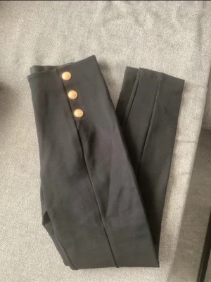 Svarta byxor med guldknappar - Stilrena svarta byxor med dekorativa guldknappar framtill.