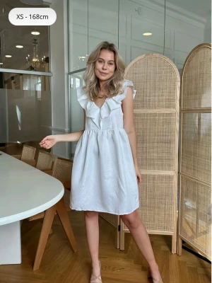 Vit klänning med volang och v-ringning - Säljer min studentklänning 💕💕 använd 1 gång! Skickar fler bilder vid intresse! Söt vit klänning med v-ringning och bred volang runt halsen. Klänningen är ärmlös och har en lätt utställd kjol i kort längd och har ett diskret mönster i tyget.