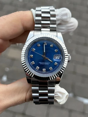 Blå klocka med silverlänk - Snygg klocka med blå urtavla och silverfärgad länk i metall. Urtavlan har glittriga indexmarkeringar och datumvisning vid klockan tre. Klassisk räfflad bezel och robust design som passar till många stilar.