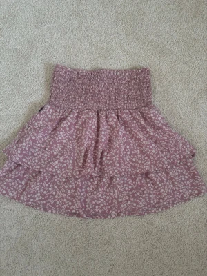 Rosa blommig volangkjol - En jättefin rosa kjol med vita blommor från Seaside i storlek 38. Den är inte så använd så därför i väldigt bra skick.