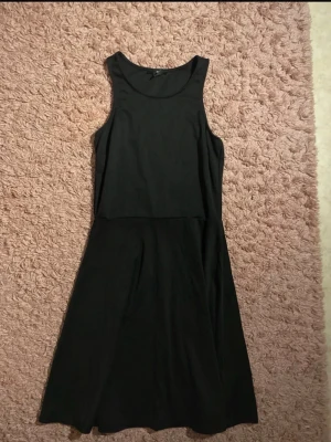 Svart ärmlös klänning från H&M - En enkel och stilren svart klänning från H&M. Klänningen är ärmlös med rund halsringning och har en lätt utställd kjol. Perfekt basplagg som kan stylas på många olika sätt. Tillverkad i mjukt och bekvämt material.