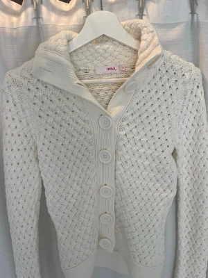 Vit stickad kofta från Zoul - Säljer en vit stickad kofta från Zoul. NYPRIS 699kr!🩷Med stora knappar framtill och ett snyggt flätmönster. Koftan har hög krage och ribbade muddar vid ärmslut och nederkant. Den passar S också! Jag skulle säga att den är S. TVEKA INTE OM FRÅGOR! Kan skicka bild på också!🌸🌼 
