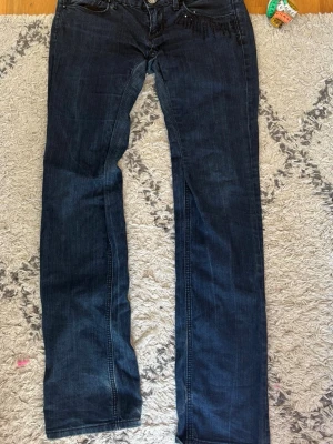 Mörkblå lågmidjade bootcut jeans med detaljer - Snygga mörkblå bootcut jeans från Fiveunits med dekorativa svarta pärlor vid fickan. Klassisk femficksmodell med knapp och dragkedja. Jeansen är i stretchigt denimtyg som sitter skönt och formar sig efter kroppen. Perfekta för dig som gillar en tidlös men trendig look.