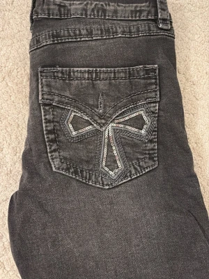 Svarta bootcut jeans med paljettdetalj - De är low waist och bootcut! De är storlek 158 men skulle säga att den passar xs och jag passade i dem när jag var ca 162! Snygga jeans med cool paljettdetalj på bakfickan i form av ett mönster. Jeansen har en lätt tvättad look och klassisk femficksmodell. Perfekta för dig som vill ha en unik touch på din outfit. Endast använd några få gånger och är ej slitna! DE ÄR SVARTA/MÖRKGRÅA