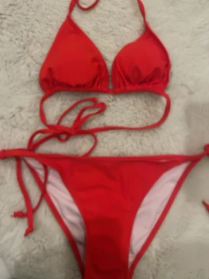Röd trekantsbikini med knyt - Snygg röd bikini med klassisk trekantsmodell och knyt i både rygg och nacke. Underdelen har knyt i sidorna för justerbar passform. Perfekt för strandhäng och soliga dagar. aldrig använt 
