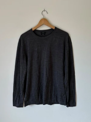 Mörkgrå Massimo Dutti långärmad tröja i merinoull - En stilren mörkgrå Massimo Dutti långärmad tröja från Arket i mjuk merinoull. Tröjan har rund halsringning och en enkel, klassisk design som passar perfekt till lager på lager eller som den är. Perfekt för dig som gillar minimalistisk stil. 6R2