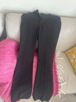 Svarta kostymbyxor med vita ränder - Säljer ett par svarta kostymbyxor med tunna vita kritstrecksränder. Byxorna har en rak passform med lätt utsvängda ben och hög midja🖤 från Bikbok! Storlek 36! 