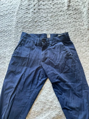 Mörkblå chinos med raka ben - Snygga mörkblå chinos med raka ben och klassisk passform. Byxorna har sidofickor fram och två bakfickor med knapp. Tillverkade i ett mjukt bomullstyg. Det står ingen stolek men skulle gissa att de passar S-M.