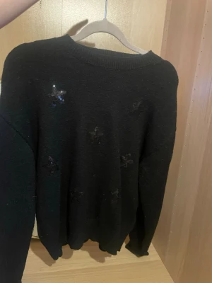 Svart stickad tröja med paljettstjärnor - Säljer en svart stickad tröja med rund hals och långa ärmar i storlek 146-152 . Tröjan har flera svarta paljettstjärnor broderade på framsidan som ger en cool och trendig look. Perfekt för dig som gillar detaljer och vill ha något extra i garderoben.skriv för fler bilder, pris kan diskuteras!💗(sitter som en xs/s)