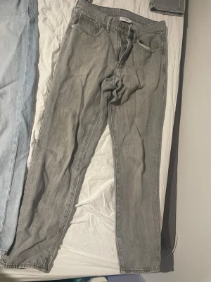 Grå raka jeans från Valient - Säljer ett par grå jeans från Weekday med rak passform och klassisk femficksdesign. Jeansen har bälteshällor, knappgylf och är tillverkade i ett slitstarkt denimtyg. Perfekta för en avslappnad och trendig look.