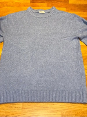 Ljusblå stickad tröja från Kappahl  - Mysig ljusblå stickad tröja från Kappahl i mjuk kashmir. Tröjan har rund halsringning, långa ärmar och ribbade muddar vid ärmslut och nederkant. Enkel och stilren design som passar perfekt till jeans eller kjol.