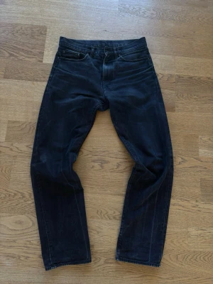 Svarta jeans från Carhartt - Säljer ett par svarta Carhartt Pontiac pants med klassisk femficksdesign och raka ben. Jeansen har en diskret logotyp på bakfickan och är tillverkade i slitstark denim. Perfekt för dig som gillar en enkel och tidlös look.