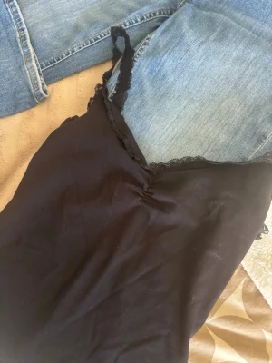 linnetopp - Snygg svart linnetopp med tunna axelband och spetsdetaljer längs urringningen. Toppen har en liten rynkning framtill som ger en fin form. Perfekt att styla med jeans eller kjol för en trendig look.