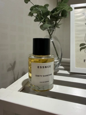 ESSNCE Dirty Dancing Eau de Parfum - ESSNCE Dirty Dancing Eau de Parfum i en stilren, rund glasflaska med svart lock. Parfymen har en ljusgul vätska och etiketten är vit med svart text. Perfekt för dig som gillar minimalistisk design och vill ha en unik doft i samlingen. 