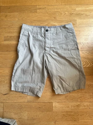 Beige bomullsshorts med fickor - Klassiska beige shorts i bomull med normal passform. De har två sidofickor fram och en bakficka med knapp. Perfekta för varma dagar och enkel stil.