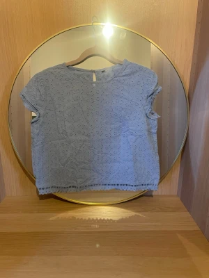 Ljusblå broderad blus med knappar  - Söt ljusblå blus med broderade hålmönster och korta ärmar. Blusen har dekorativa knappar i ryggen och en fin spetskant längst ner. Perfekt för dig som gillar detaljer och en luftig stil.vet ej vart den kommer ifrån. Pris kan diskuteras!💗(skulle säga att den sitter som en xs/s)