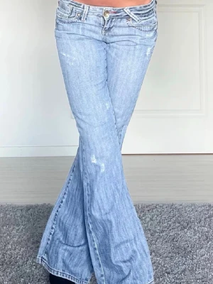 Ljusblå lågmidjade bootcut jeans cross jeans - Säljer ett par ljusblå bootcut jeans från cross jeans med slitna detaljer och broderade bakfickor. Jeansen har låg midja, klassisk femficksmodell och är tillverkade i denim med stretch. Perfekta för en avslappnad och trendig look.
