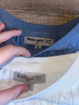 Två kabelstickade tröjor Basic You - Säljer två kabelstickade tröjor från Basic You i storlek S. En är ljusblå och en är vit, båda i ekologisk bomull. Klassisk rund halsringning och ribbade muddar vid ärmslut och nederkant. Kontakta vid frågor, en kostar 60 kr båda för 100
