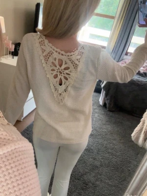 Vit stickad tröja med spetsdetalj - Säljer en vit stickad tröja med lång ärm och unik virkad spets i ryggen som bildar ett V och ett blommönster. 