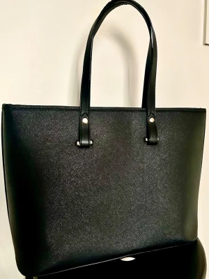 Svart H&M Shopper 🖤 Perfekt som skolväska/datorväska! - Säljer min klassiska shopper från H&M i svart läderimitation. Den är rymlig och passar perfekt för dig som behöver få plats med laptop (upp till 15"), block och annat för skolan eller jobbet! 💻✨ Detaljer: Dragkedja upptill så allt ligger säkert, samt ett mindre innerfack med blixtlås för småsaker. Mått: 42cm bred upptill & 30cm hög. Skick: Väskan är superfin och fräsch invändigt! Det finns lite naturligt slitage på handtagens kanter