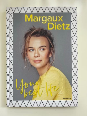 Your Best Life av Margaux Dietz - En ny, oanvänd och  inspirerande bok av Margaux Dietz med titeln 'Your Best Life'. Omslaget har ett grafiskt svartvitt mönster och en porträttbild med gul text. Perfekt för dig som gillar personlig utveckling och skönlitteratur. Inbunden bok med mycket privata bilder i boken. Läs den!