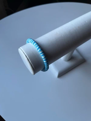 Blåvitt armband  -  Ett somrigt blåvitt armband som har elastiskt band så att det är lätt att ta på och av och har även ett guldlås så att man kan också knäppa armbandet. Armbandet är handgjort.