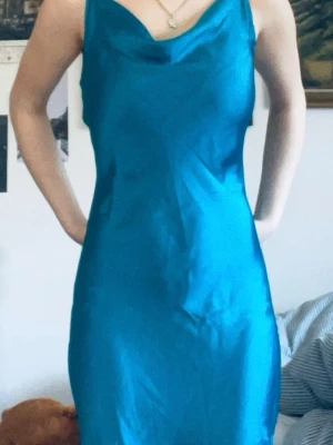 Balklänning  - Säljer en elegant turkos långklänning med tunna axelband och mjukt, glansigt tyg. Klänningen har en smickrande passform och enkel, stilren design som ger en lyxig känsla. Perfekt till balen och har en en väldigt smickrande passform. Den har vissa väldigt små defekter men det är inget man lägger märket till