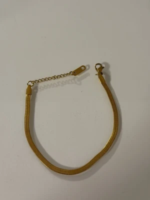 Guldigt kedjearmband med justerbar längd - Snyggt armband i guldfärgad metall med slät, ormliknande kedja och justerbar kedjeförlängning. Perfekt för att ge en stilren touch till din outfit. Enkel karbinhake för smidig användning.
