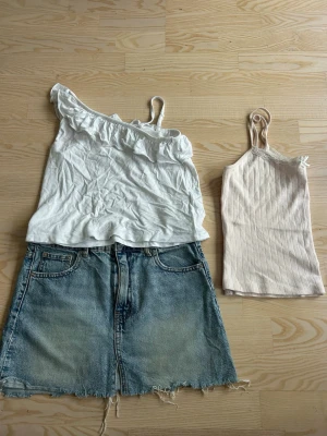 Vit oneshoulder topp med volang, jeansshorts  - Snygg vit topp med oneshoulder och volangdetalj längs axeln. Perfekt för dig som gillar en trendig och feminin stil. Tunt och mjukt material som känns skönt mot huden.