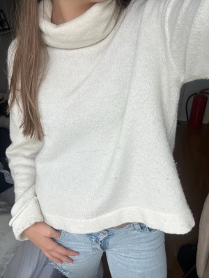 Vit polotröja i stickat material - Mysig vit stickad polotröja med bred krage och avslappnad passform. Tröjan har långa ärmar och ribbade muddar, perfekt för lager på lager. Passar till jeans eller kjol för en chill look.