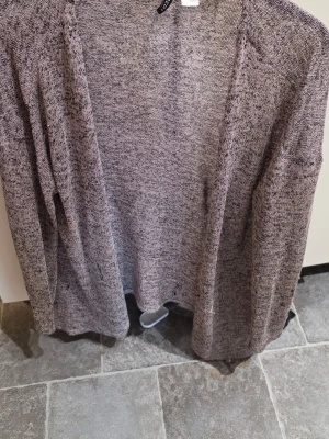 Gråmelerad öppen kofta Divided - Säljer en tunn, gråmelerad öppen kofta från Divided. Koftan har lång ärm och är tillverkad i ett mjukt, lätt material som passar perfekt för lager på lager. Enkel och stilren design utan knappar eller dragkedja.