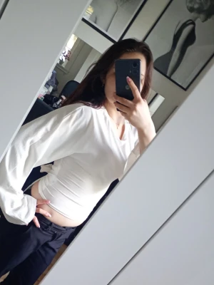 Vit långärmad topp med vida ärmar - Säljer en vit långärmad topp med vida ärmar och rund halsringning den är lite för stor på mig och därför händer urringning ner lite.Toppen har en croppad passform och knyts på baksidan av tröjan. är enkel att matcha med olika outfits. Perfekt för dig som gillar stilrena och trendiga plagg.💗🪷