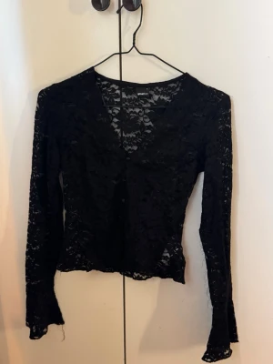 Svart spetstopp från Gina Tricot - Säljer en svart långärmad spetstopp från Gina Tricot. Blusen har v-ringning och är genombruten med blommigt spetsmönster. Perfekt att styla lager på lager eller med ett linne under. Snygg och trendig topp för dig som gillar detaljer.